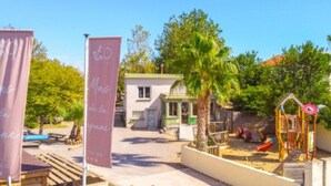 A playground with a slide and climbing structures, surrounded by trees and a building with a green roof. - Mobile-home with AC - 4 guests (Frontignan)