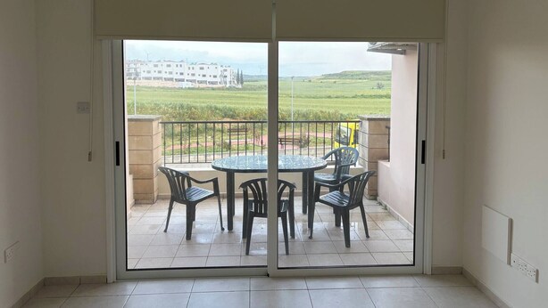 Ein Balkon mit Tisch und Stühlen, eine Schiebetür und Blick auf ein Gebäude und Felder.