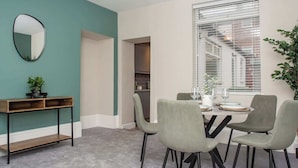 A dining area with a round table, four chairs, a console table with a mirror, and a potted plant.