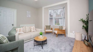 A living room with a sofa, chairs, a coffee table, a door, and a window with blinds.