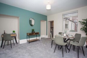 En moderne stue med teal vægge, et spiseområde med grå stole, et sofabord og et stort vindue med persienner.