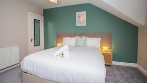 A bedroom with a sloped ceiling, a bed with white linens, a bedside table with a lamp, and a framed picture on the wall.