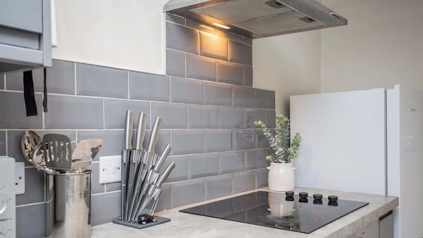 A modern kitchen with grey tiles, stainless steel utensils, a gas stove, and a white refrigerator.