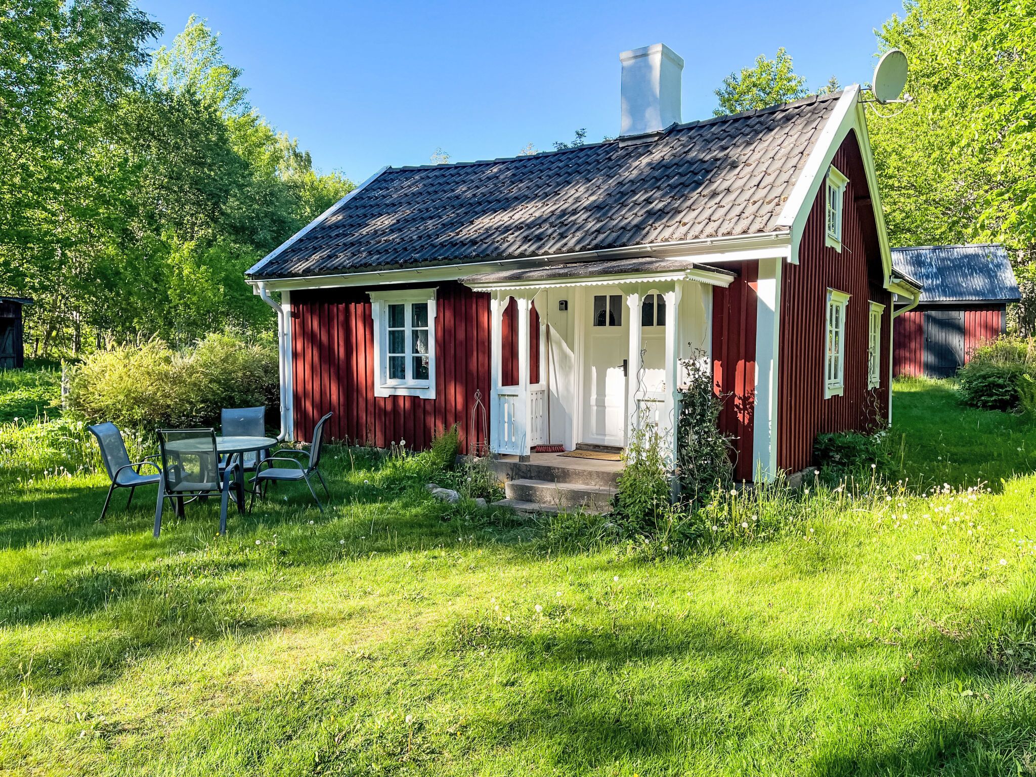 Ett rött trähus med en vit veranda, en skorsten och en satellitparabol.