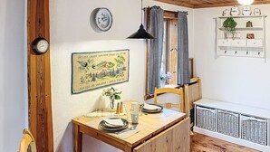 Un comedor con una mesa de madera, sillas, un jarrón con flores, un reloj de pared, un cuadro enmarcado y un aparador blanco con estantes.