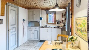 Una cocina con armarios blancos, techo de madera y una mesa de comedor dispuesta con platos, tazas y un florero.