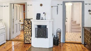 Una habitación con chimenea, suelo de madera, una escalera y una puerta que da a otra estancia.