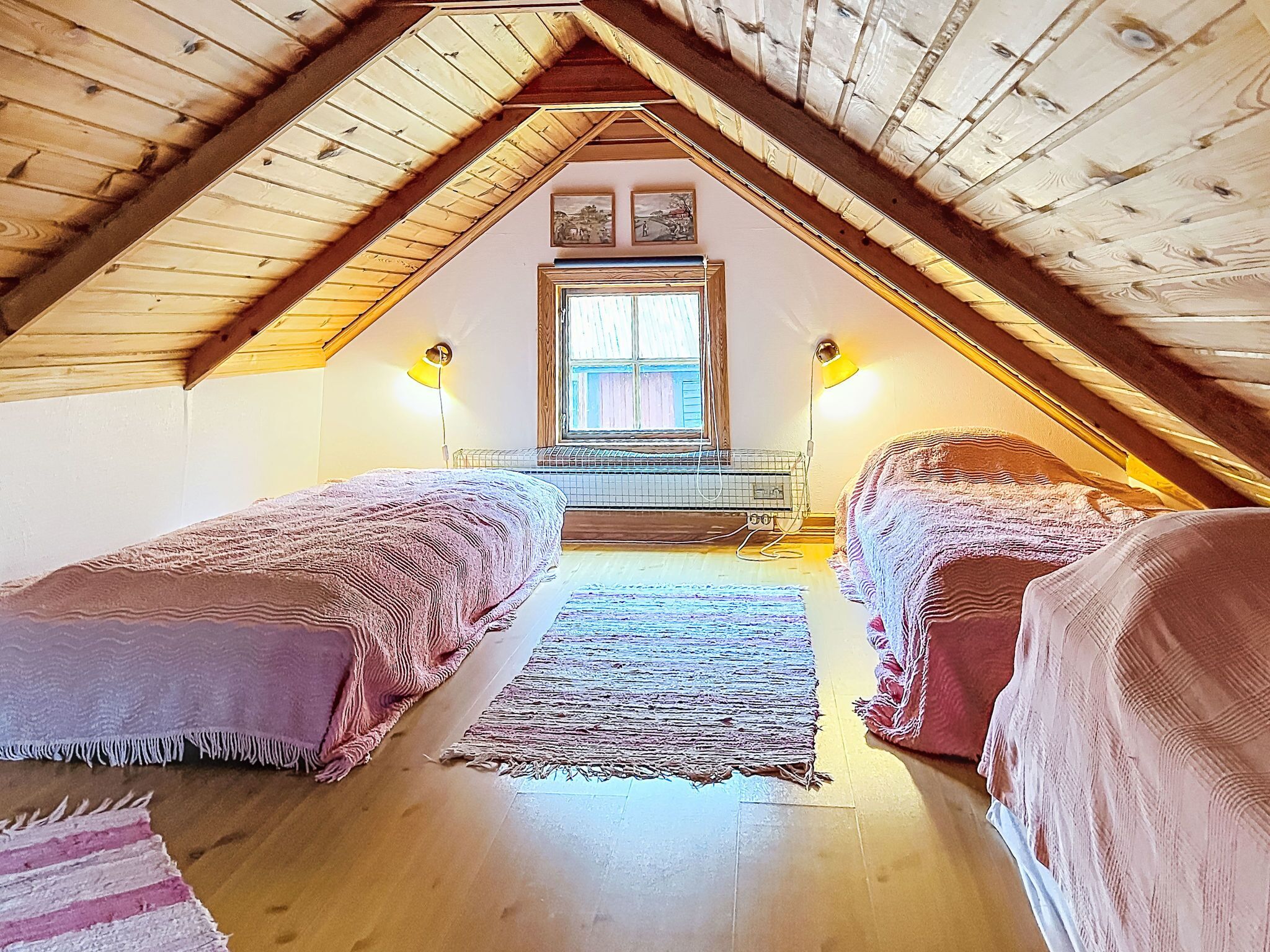 An attic bedroom with two beds, a window, and a wooden ceiling.