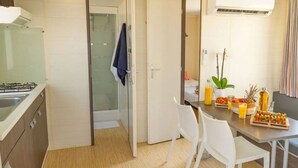 A compact kitchen with a gas stove, a glass shower, and a dining area with a table set for two. - Mobile home - AC - 4 guests (Frontignan)
