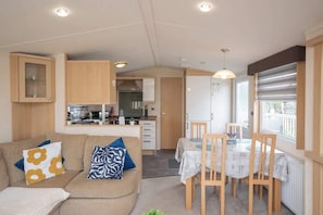 Un espace de vie compact comprenant un coin cuisine, un coin repas et un canapé agrémenté de coussins à motifs.