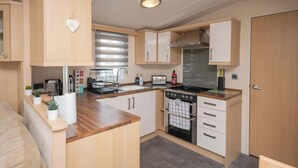 Cocina compacta con muebles de madera, horno integrado y encimera con diversos electrodomésticos.