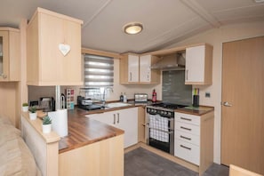 Cocina compacta con muebles de madera, horno integrado y encimera con diversos electrodomésticos.