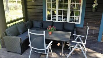Een terras buiten met een donkergrijze bank, een klein rond tafeltje en witte stoelen.