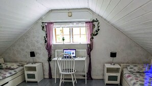 Una piccola camera da letto mansardata con un soffitto spiovente, una scrivania con un computer, una sedia, due comodini e un letto.