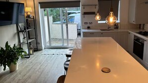 Ett modernt kök med en stor köksö, hängande lampor och en skjutdörr i glas som leder ut till en uteplats.