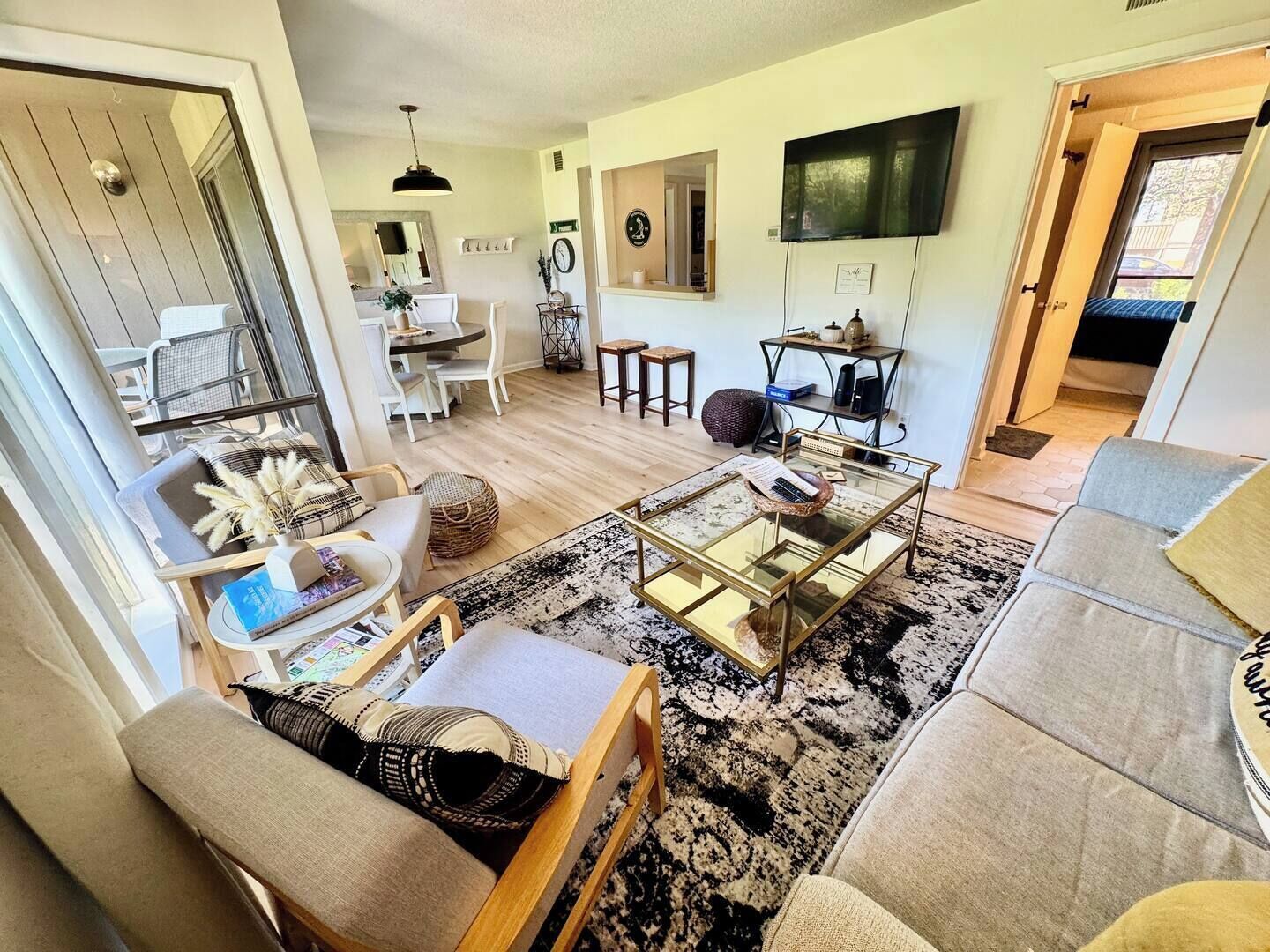 A living room with a sofa, coffee table, and chairs. There is a dining area with a table and chairs, and a kitchen area with a counter and appliances.