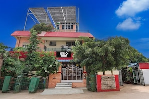 Un hotel con techo rojo, paneles solares, entrada protegida por un portón y un cartel.