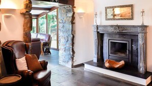 A stone pillar, a fireplace with a mirror, a leather armchair, and a view through a glass door. - Luxury Ardennes Villa With Pool and Sauna (Stoumont)