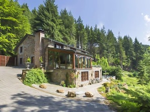 A stone house with large windows, surrounded by dense forest. - Luxury Ardennes Villa With Pool and Sauna (Stoumont)