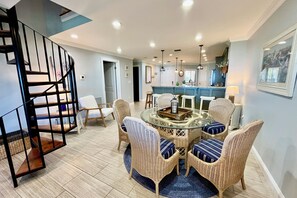 Un coin repas avec des chaises en osier, une table en verre et un escalier.