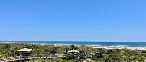 A beach view with a wooden boardwalk, a gazebo, and a beach area with umbrellas.