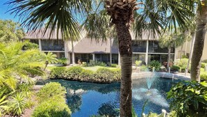 A pool surrounded by lush greenery and a modern building with large windows. - Modern Gold-rated beach chic condo with views of bubbling lagoon! (Saint Augustine)