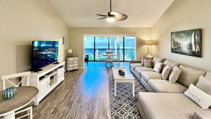 A living room with a TV, sofa, coffee table, and a view of the outdoors. - Modern Gold-rated beach chic condo with views of bubbling lagoon! (Saint Augustine)