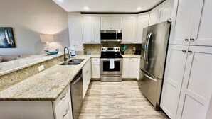 A modern kitchen with white cabinets, stainless steel appliances, granite countertops, and a tiled backsplash. - Modern Gold-rated beach chic condo with views of bubbling lagoon! (Saint Augustine)