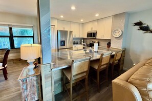 A modern kitchen with white cabinets, stainless steel appliances, a large island, and a dining area with wooden chairs. - Enjoy upgraded amenities in this stunning Gold-rated condo with views overlooking the pool and ocean. (Saint Augustine)