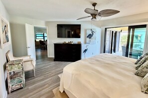 A bedroom with a bed, a ceiling fan, a TV, a dresser, and a view of the outdoors. - Enjoy upgraded amenities in this stunning Gold-rated condo with views overlooking the pool and ocean. (Saint Augustine)