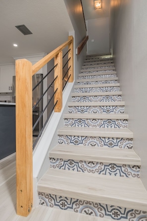 Eine Treppe mit gemusterten Stufen, einem Holzgeländer und einer modernen Küche im Hintergrund.