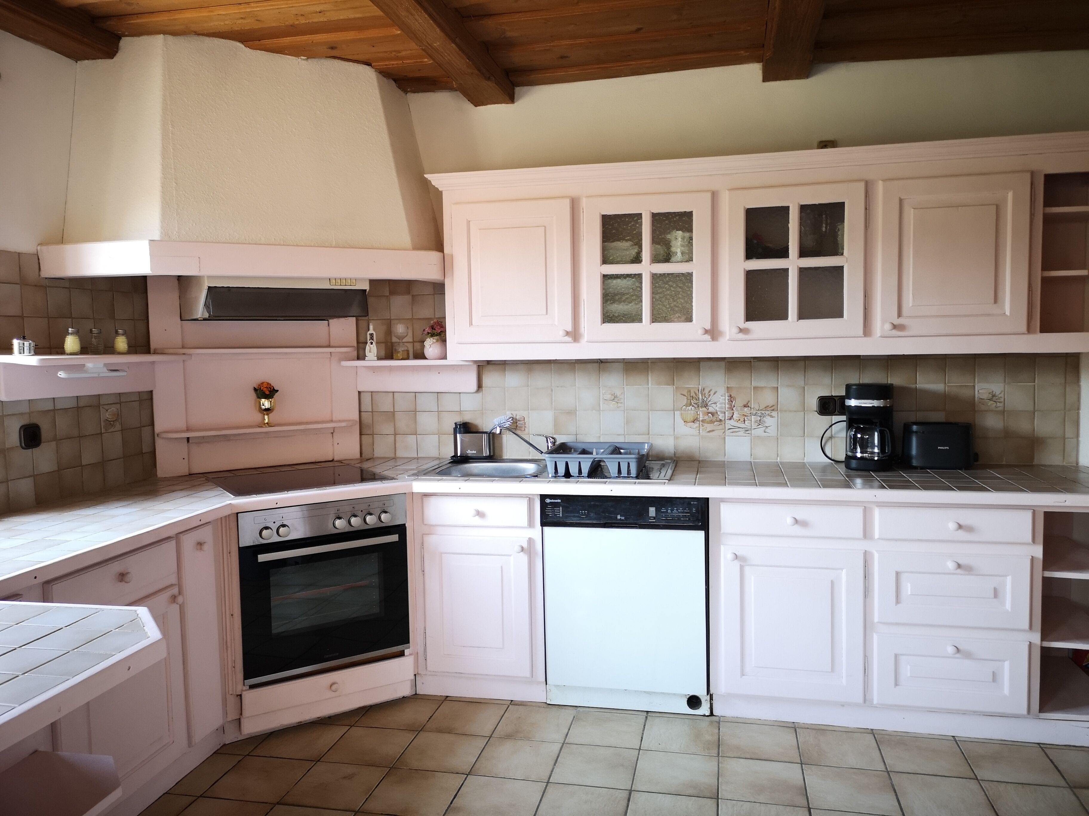 Una cocina con armarios blancos, estufa, horno, lavavajillas y cafetera.