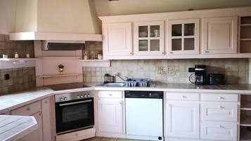 Una cocina con armarios blancos, estufa, horno, lavavajillas y cafetera.