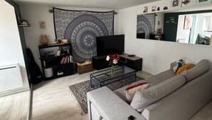 Un salon moderne avec un canapé gris, une table basse en verre, un téléviseur et une tapisserie au mur.
