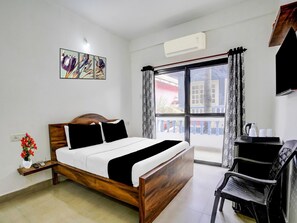 Une chambre d’hôtel avec un lit en bois, un bureau avec une chaise, une fenêtre avec des rideaux et un climatiseur fixé au mur.