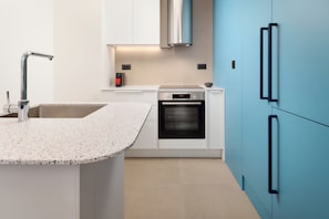 Une cuisine moderne dotée d’un comptoir en granit, d’appareils électroménagers en acier inoxydable et de meubles de couleur bleue.