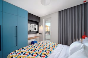 A modern hotel room with a bed, a blue wardrobe, a small desk, and a view of the outside. - Superior apartment with balcony (Split)