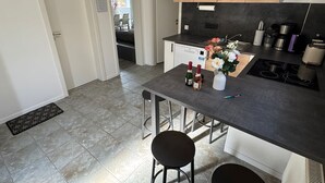 A modern kitchen with a central island, bar stools, a built-in stove, and a dining area with chairs. - Cozy quiet apartment in Berlin with terrace, free parking (Berlin)