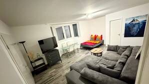 A modern living room with a sofa, a TV, a dining table, and a bed. - Cozy quiet apartment in Berlin with terrace, free parking (Berlin)