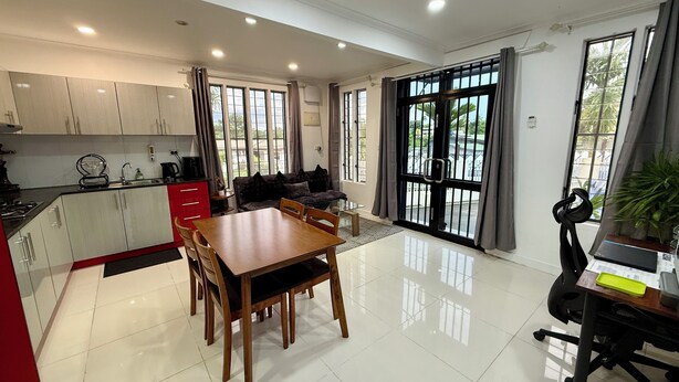 A modern kitchen with white cabinets, a dining table with chairs, a sofa, and large windows with curtains. - 1 Bedroom Apartment in Namadi Height, SUVA (Suva)