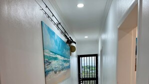 A hallway with a tiled floor, a painting of a beach scene, a ceiling light, and a door with a barred window. - 1 Bedroom Apartment in Namadi Height, SUVA (Suva)
