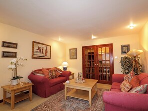 A living room with a red sofa, a wooden coffee table, a floor lamp, and a patterned rug. - Dunhallin House (Inverness)
