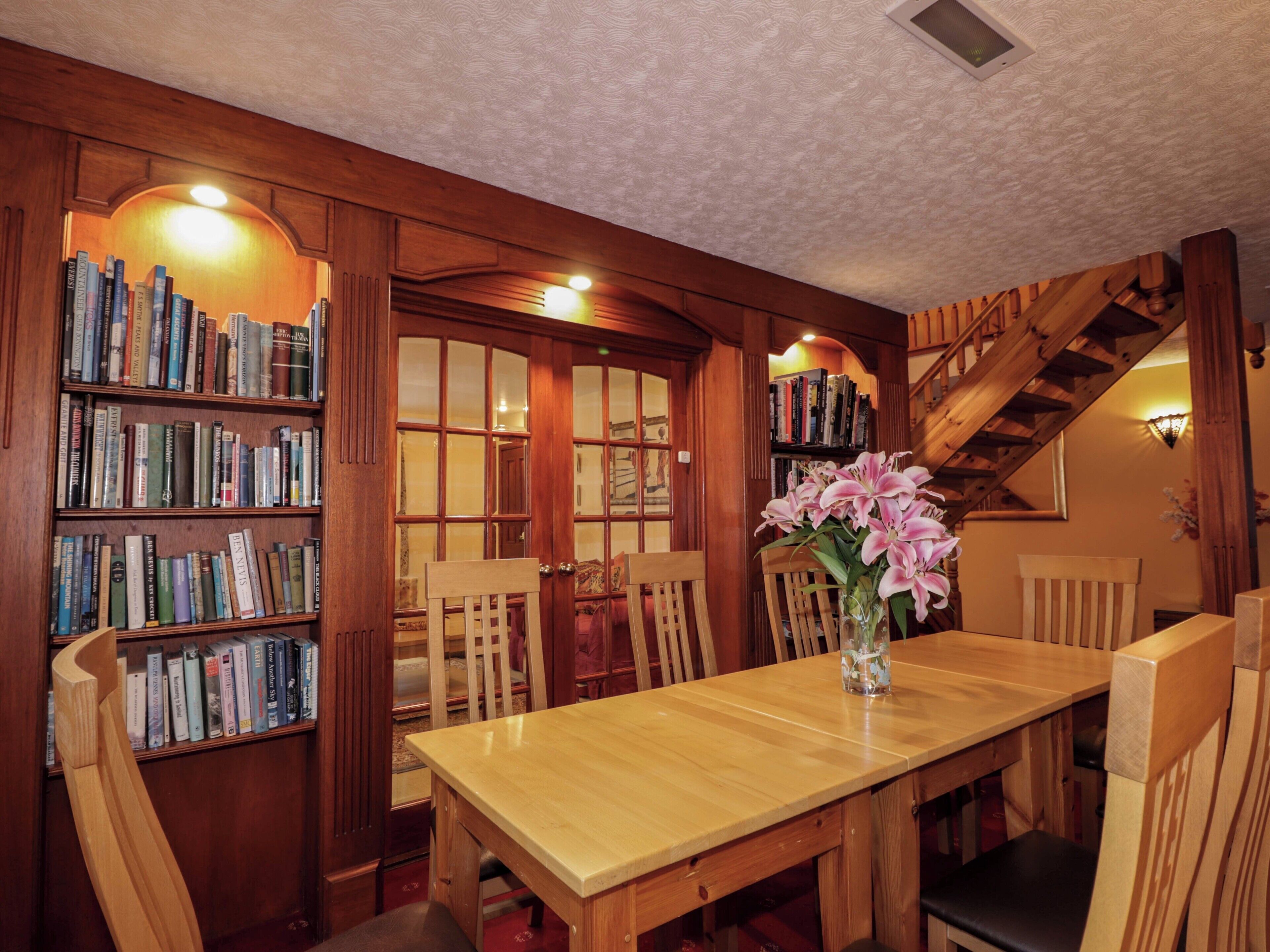 Una biblioteca de madera con estanterías, una mesa de comedor, sillas y una escalera.