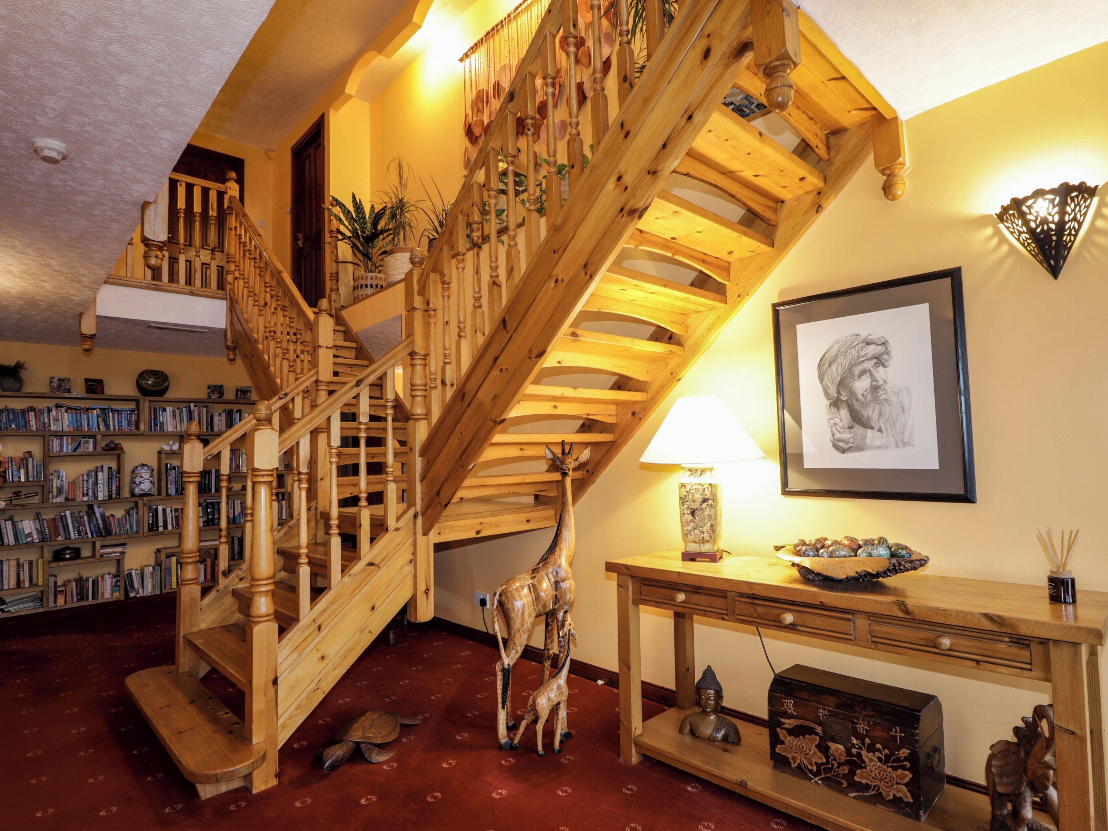 Una escalera de madera con una estantería y una obra enmarcadas en la pared.