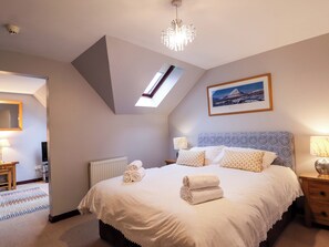 A bedroom with a skylight, a bed with rolled towels, a bedside lamp, a framed picture, and a radiator. - Dunhallin House (Inverness)