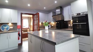 A modern kitchen with white cabinets, a granite countertop, a built-in oven, and a microwave. - Dunhallin House (Inverness)