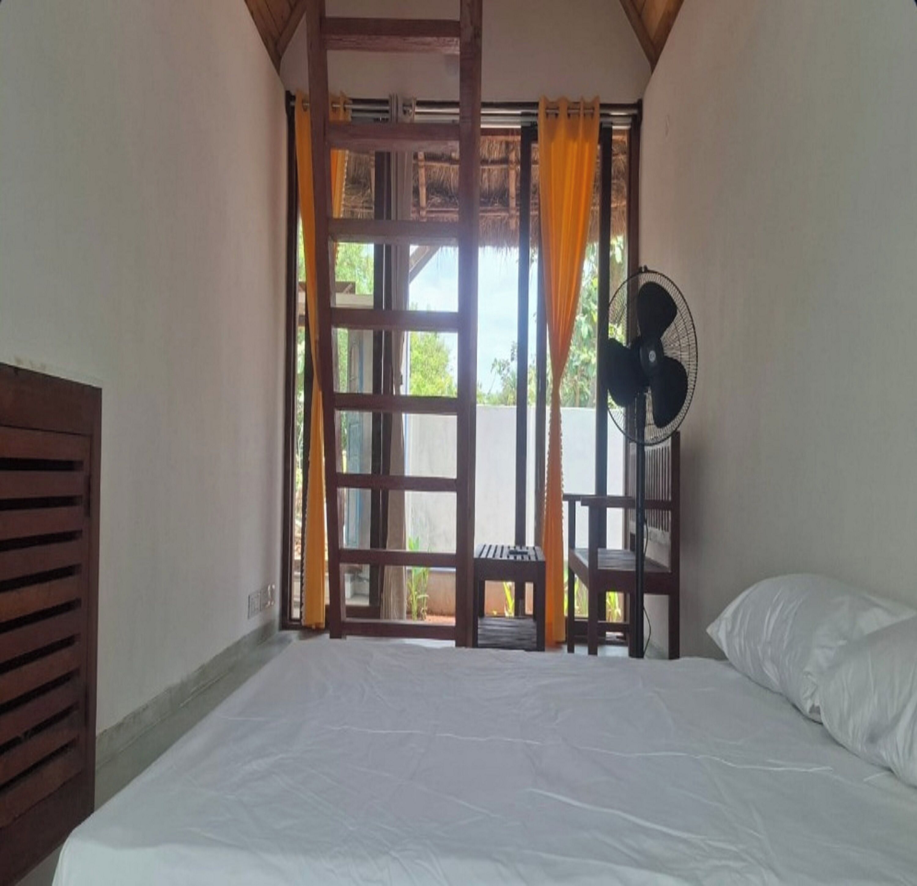 A room with a bed, a fan, and a window with curtains.