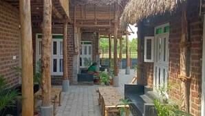 A courtyard with thatched-roof structures, potted plants, and a paved walkway. - Huts Life Home Stay (Vanur)