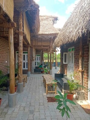 A courtyard with thatched-roof structures, potted plants, and a paved walkway. - Huts Life Home Stay (Vanur)