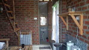 A rustic kitchen with a brick wall, wooden beams, a sink, and a table with mugs. - Huts Life Home Stay (Vanur)